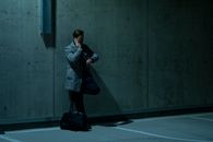 Adult man in coat on phone checks wristwatch in dim parking setting.