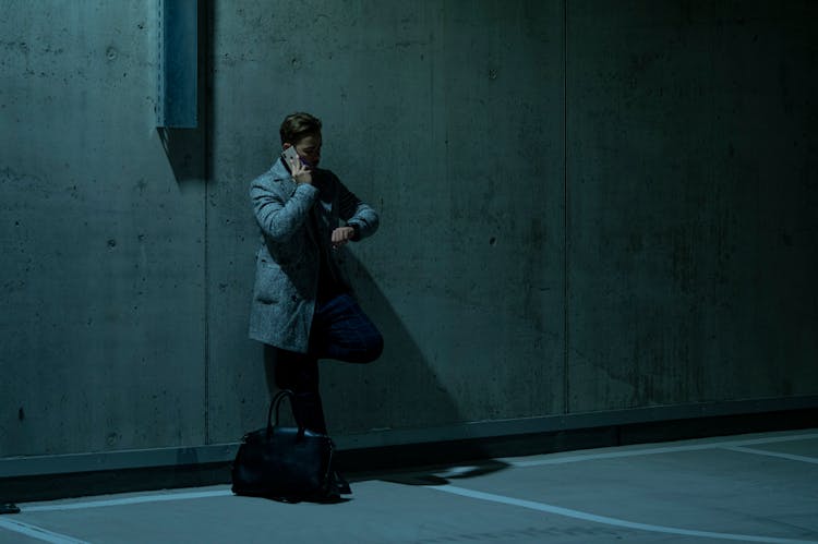 Man On Phone Call Leaning On Wall And Looking At His Watch