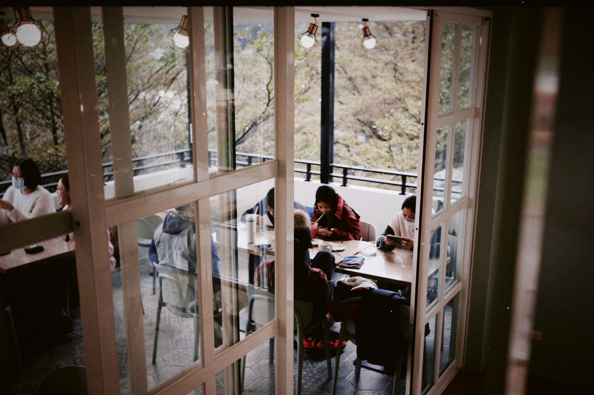 A lively group enjoys a meal on a balcony with French doors under ambient lighting.