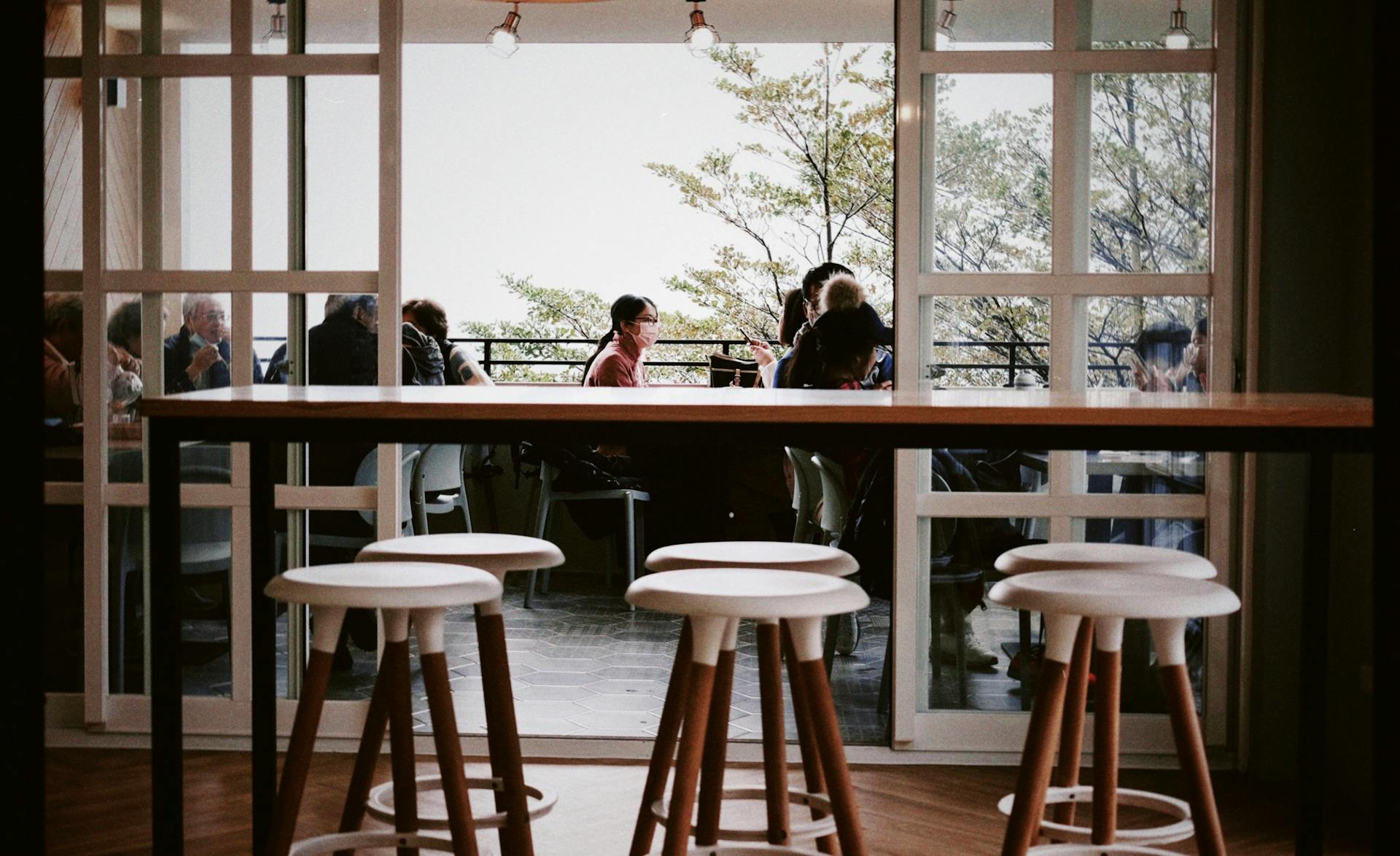 Stylish café interior with stools and a view of outdoor seating area with people.