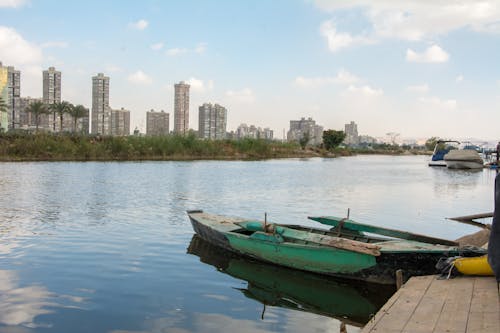 Green Wooden Boat on Water Near City Buildings