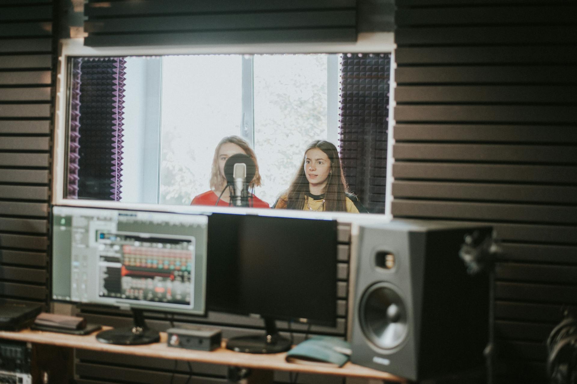 Two women recording music in a professional studio with microphone and speakers, showcasing vocal performance.