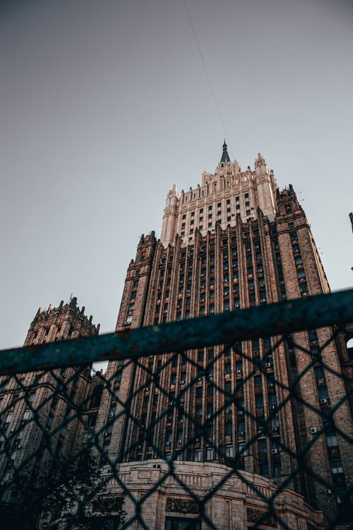 Free Low-angle view of Moscow's gothic skyscraper behind a chain link fence under a gray sky. Stock Photo