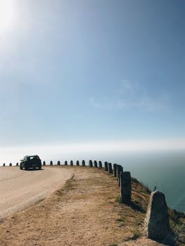 An automobile on a picturesque coastal road overlooking the ocean on a bright sunny day.
