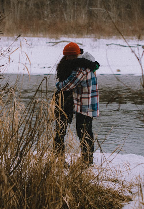 Couple Hugging While Standing by the Water in Winter 