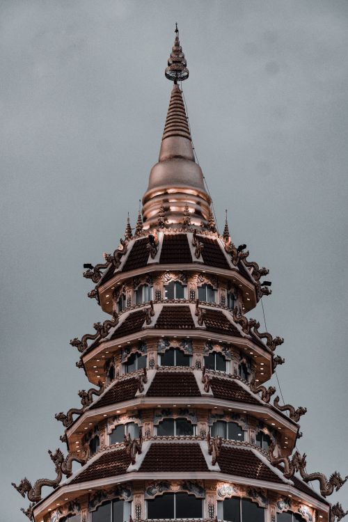 Free Vertical shot of an intricate Buddhist pagoda with ornate designs against a gray sky. Stock Photo
