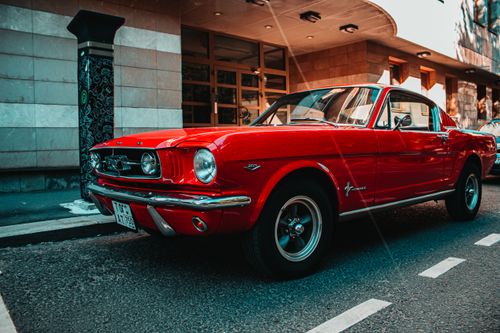 Free A stunning vintage red Ford Mustang captured in a vibrant city street setting. Stock Photo