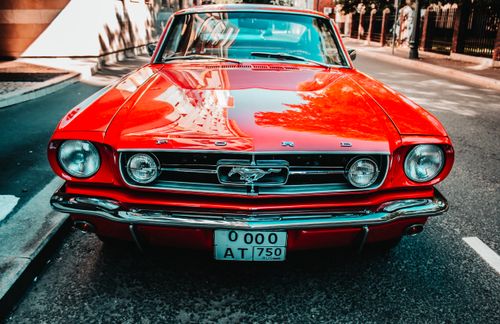 Free Front view of a vintage red Ford Mustang parked on a city street, highlighting classic design. Stock Photo