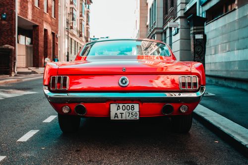 Free Classic red Ford Mustang parked on a city street, showcasing its iconic rear design. Stock Photo