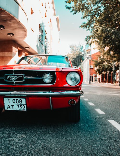 Free Iconic red Ford Mustang parked on a sunny urban street with classic architecture. Stock Photo