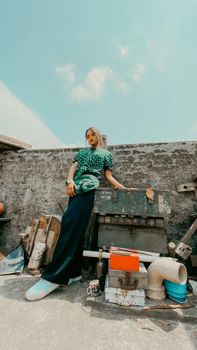 Woman in stylish outfit posing against urban backdrop with scrap materials.