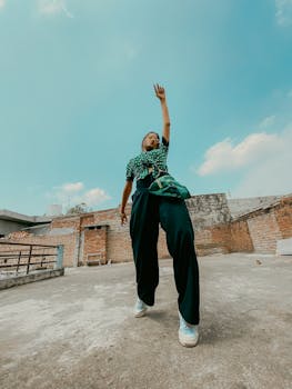 Low angle shot of woman in green attire reaching towards the sky on a sunny rooftop.