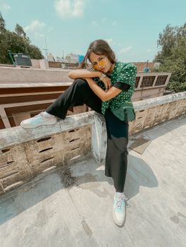 Stylish young woman wearing sunglasses, posing casually on a sunny rooftop day.
