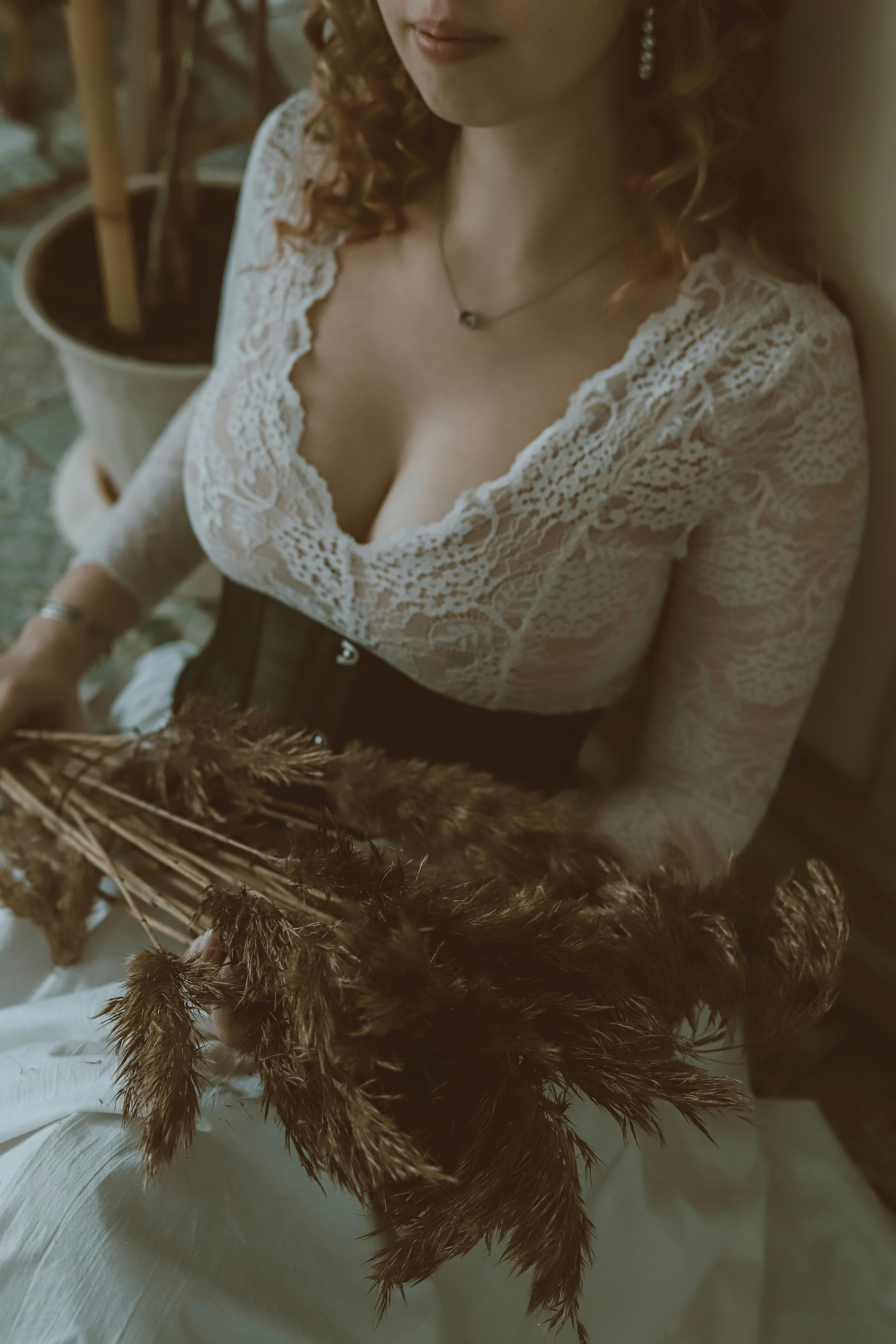A woman in a white lace dress holding dried plants indoors, with a warm and vintage mood.