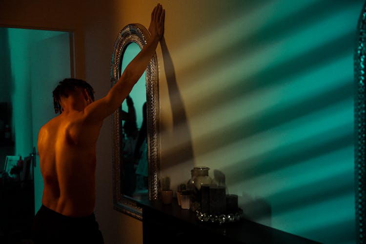 A Shirtless Man Touching The Wall While Facing The Mirror