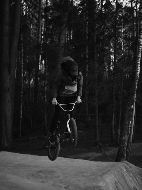A Grayscale Photo of a Man Riding Bicycle in the Forest
