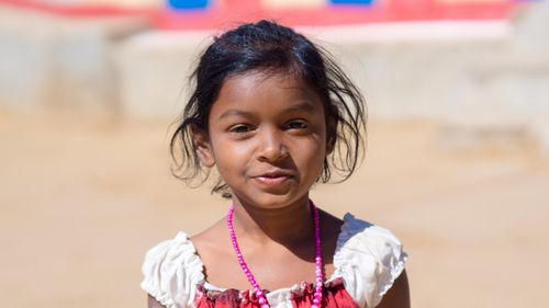 Free A heartwarming outdoor portrait of a young girl wearing a colorful beaded necklace and smiling under the sun. Stock Photo