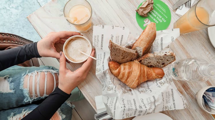 Person Holding A Cup Of Coffee Beside Pastries