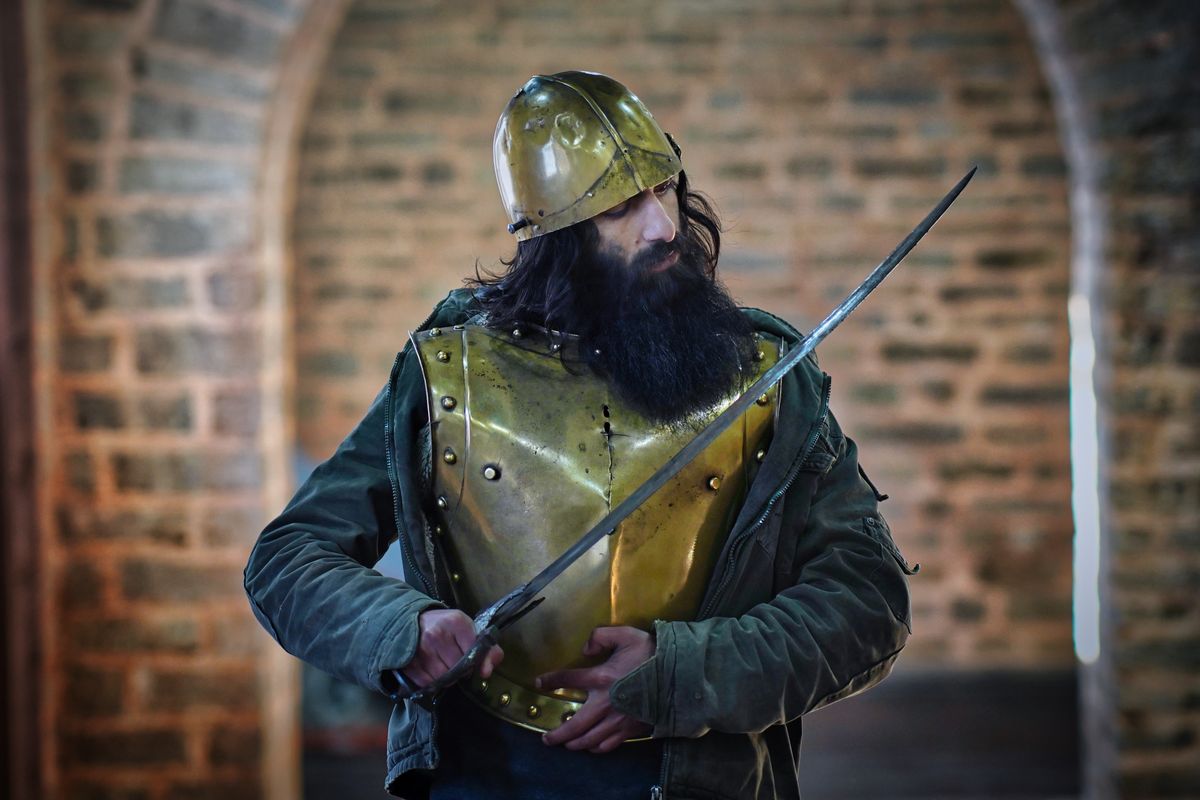 A medieval knight in protective armor holding a sword in a historic stone setting.