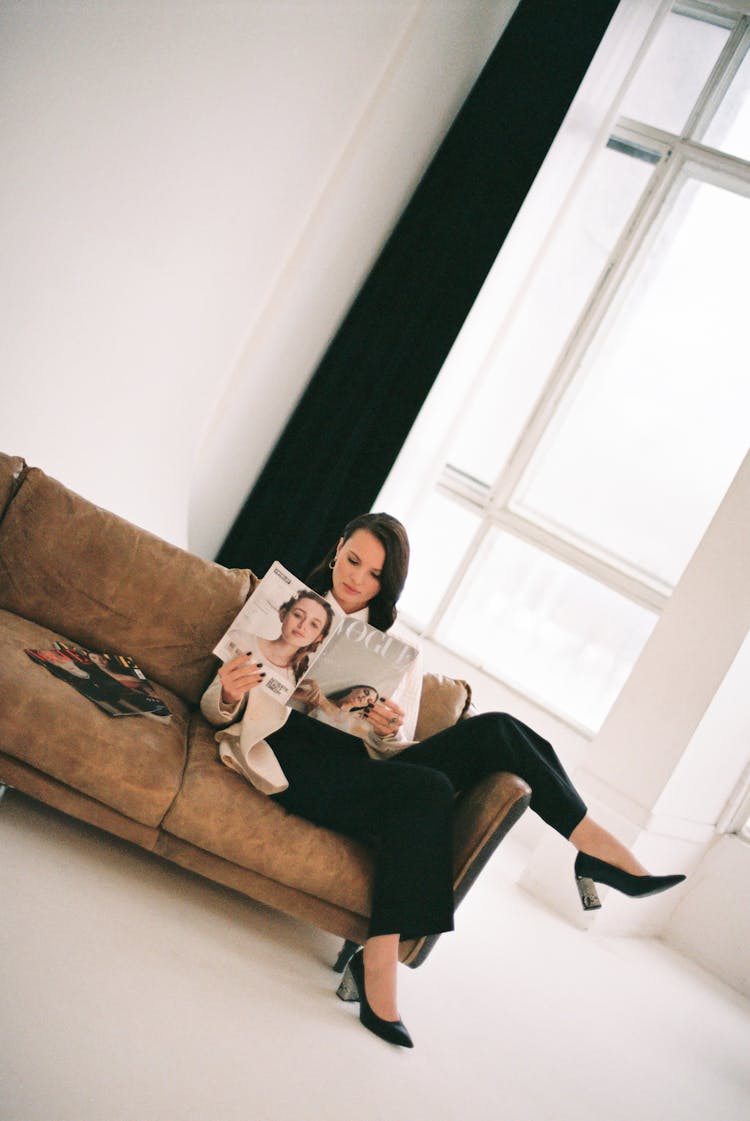 Woman Sitting On Brown Couch While Reading A Vogue Magazine