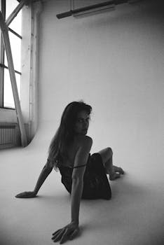 Black and white portrait of a woman in lingerie sitting on a studio floor, displaying sensuality.