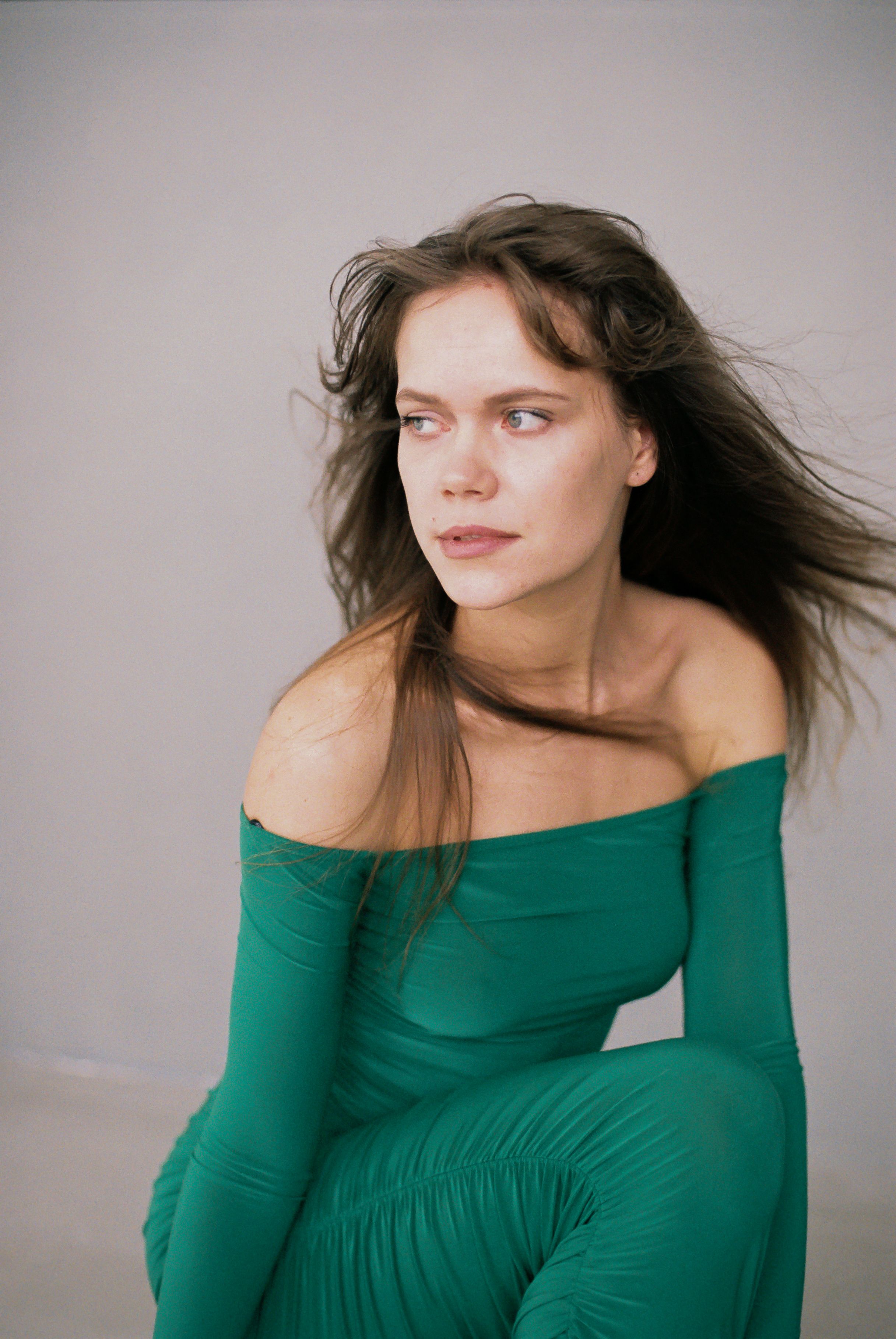 Portrait of an elegant woman in a green off-shoulder dress with flowing hair.