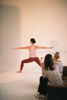 A woman performing a yoga pose indoors photographed by others in a studio environment.