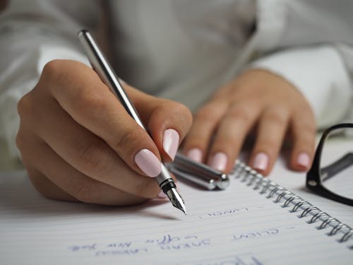 紙に書くペンを持っている白い長袖シャツの女性