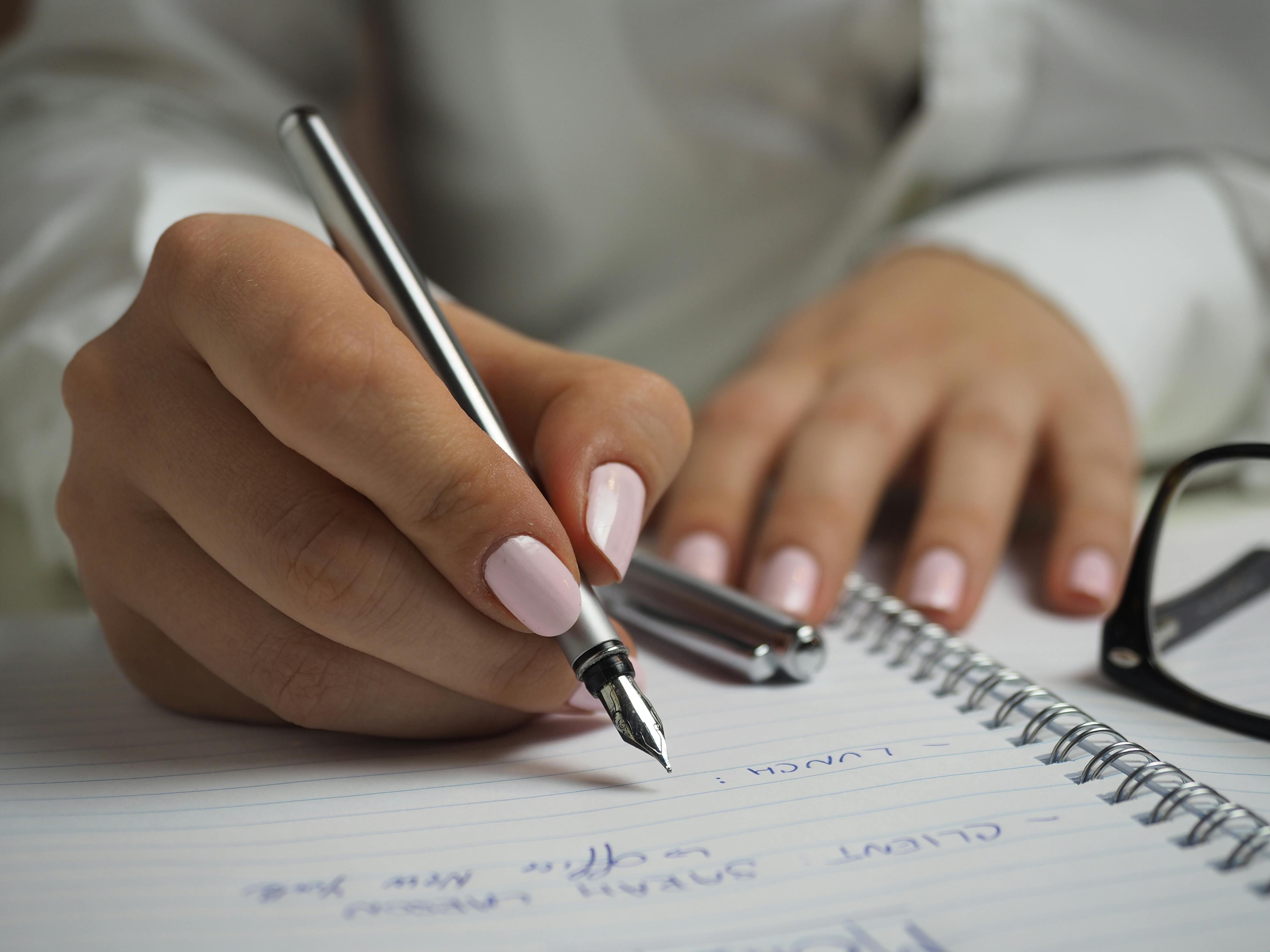 紙に書くペンを持っている白い長袖シャツの女性 無料の写真素材