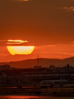 A vibrant sunset illuminating an airport scene with silhouettes of airplanes and distant hills.