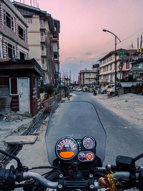 Free POV of motorcycle riding through a quiet town street at sunset with distant mountains. Stock Photo