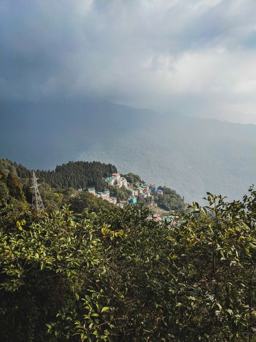 Free Aerial view of a peaceful mountain village surrounded by lush greenery under a moody sky. Stock Photo