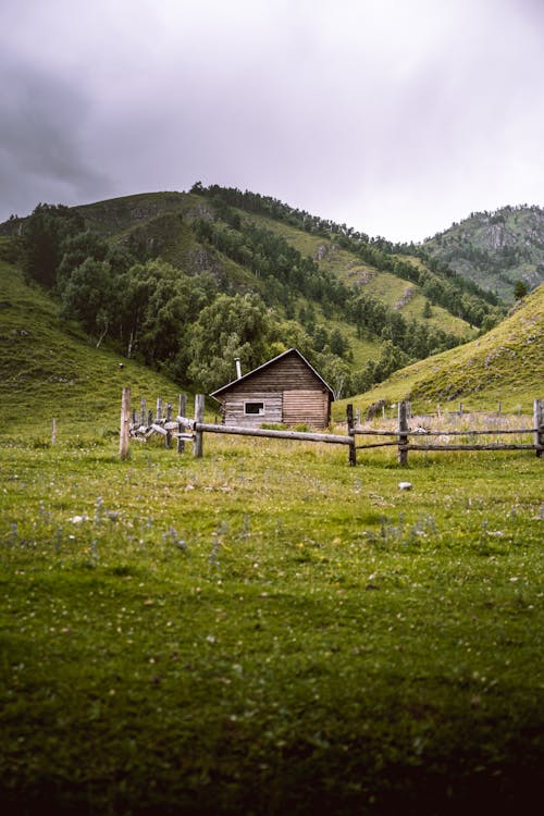 A Brown Wooden House on Green Grass Field Near Green Mountain