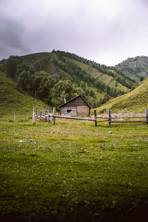 Free Scenic view of a wooden cabin amidst lush greenery and rolling hills. Stock Photo