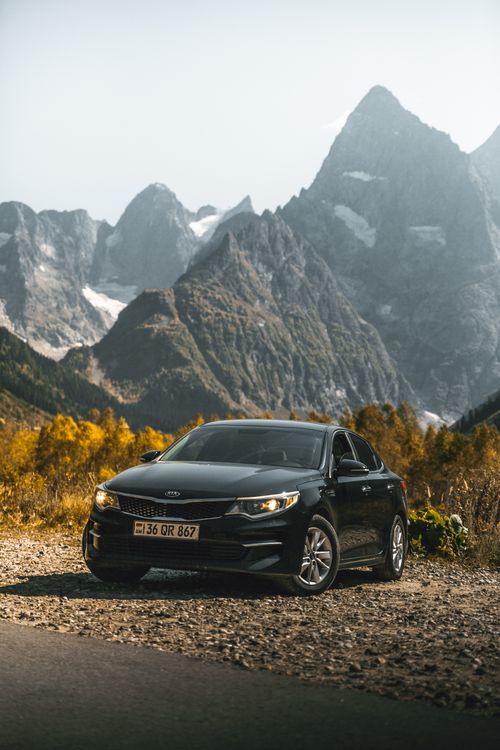 Free Black sedan parked on rocky terrain with towering mountains in the background, showcasing nature's grandeur. Stock Photo