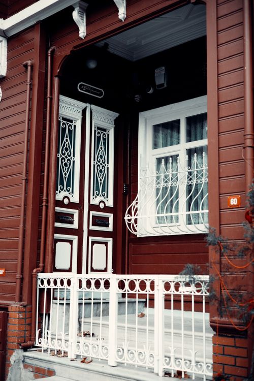Free Elegant wooden facade featuring an ornate white door and window grille. Stock Photo
