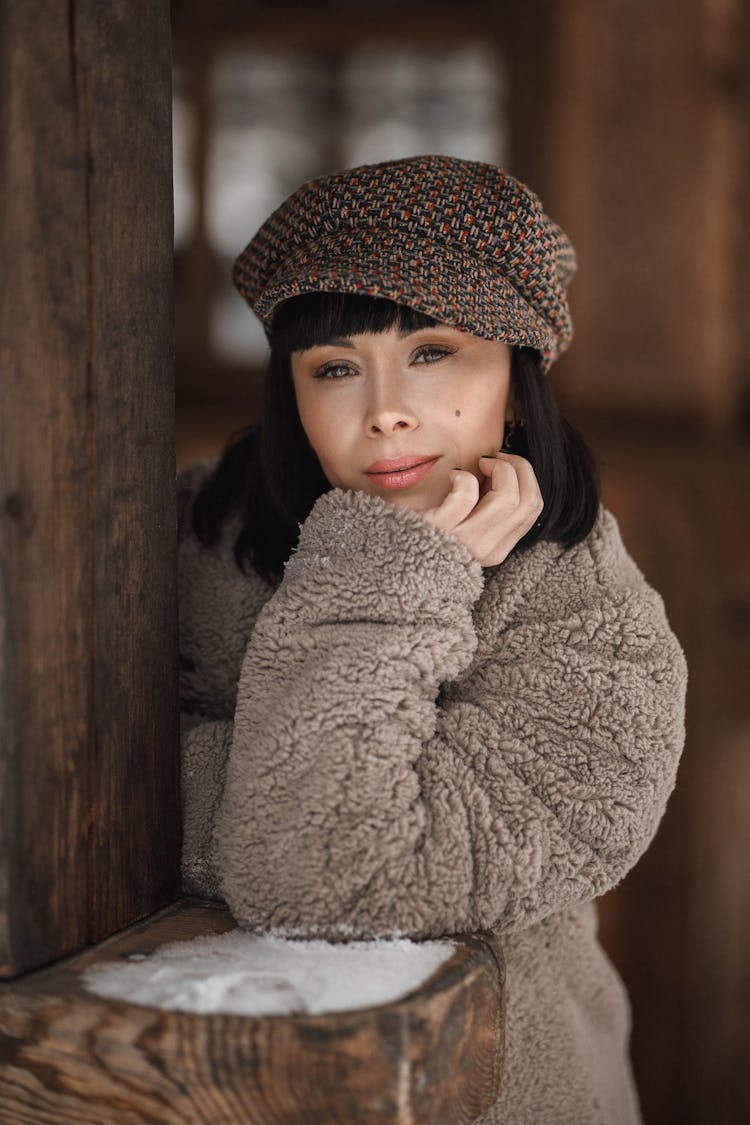 Woman Wearing Winter Coat And Gavroche Cap Leaning On Wooden Beam