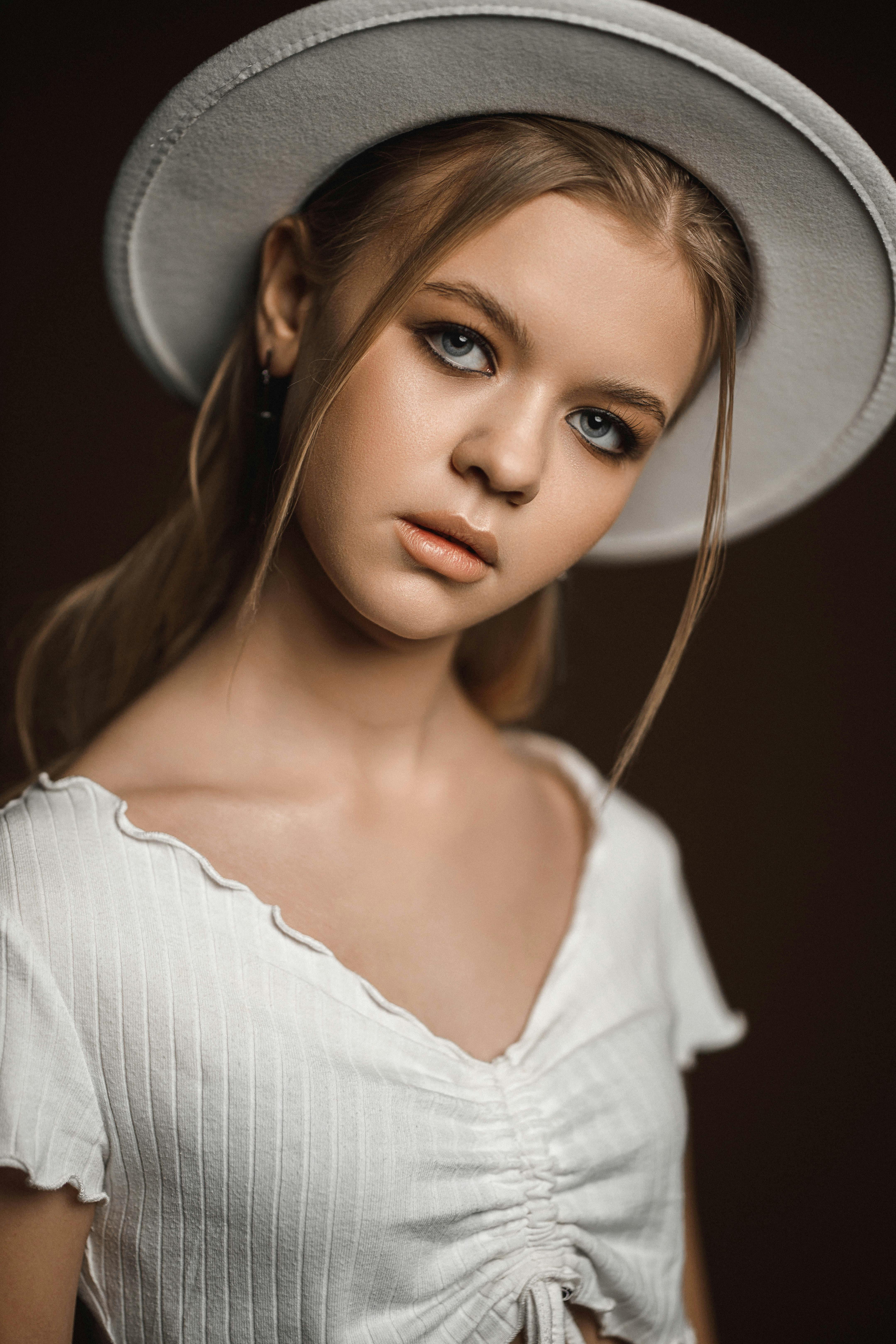 teenage blond girl in white short top and hat on tilted head