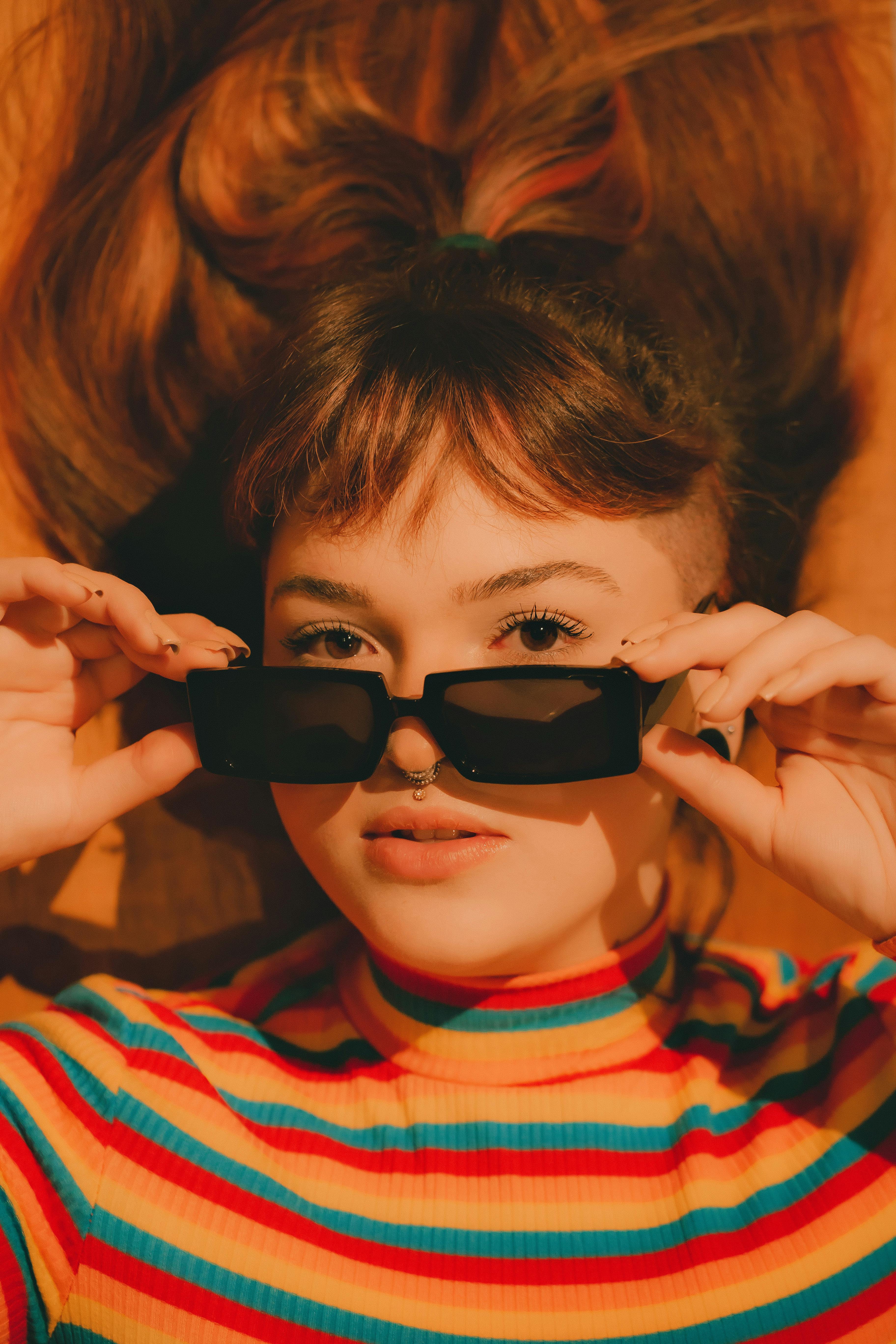 teenage girl wearing coloured striped blouse laying on back with sunglasses in hands