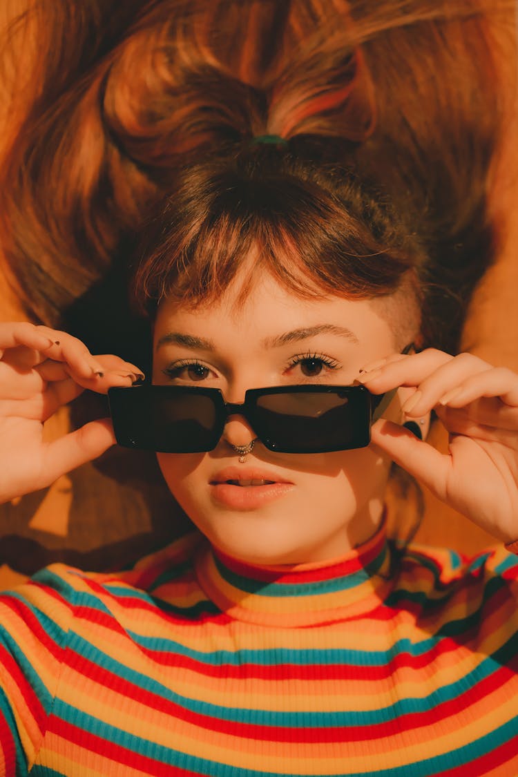 Teenage Girl Wearing Coloured Striped Blouse Laying On Back With Sunglasses In Hands