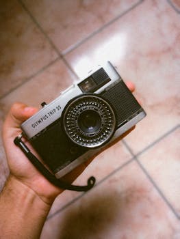 Close-up of a person holding a classic Olympus Trip 35 film camera, emphasizing retro style.