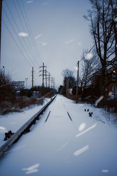 A serene winter scene with snow-covered railway tracks and utility poles lining the path.