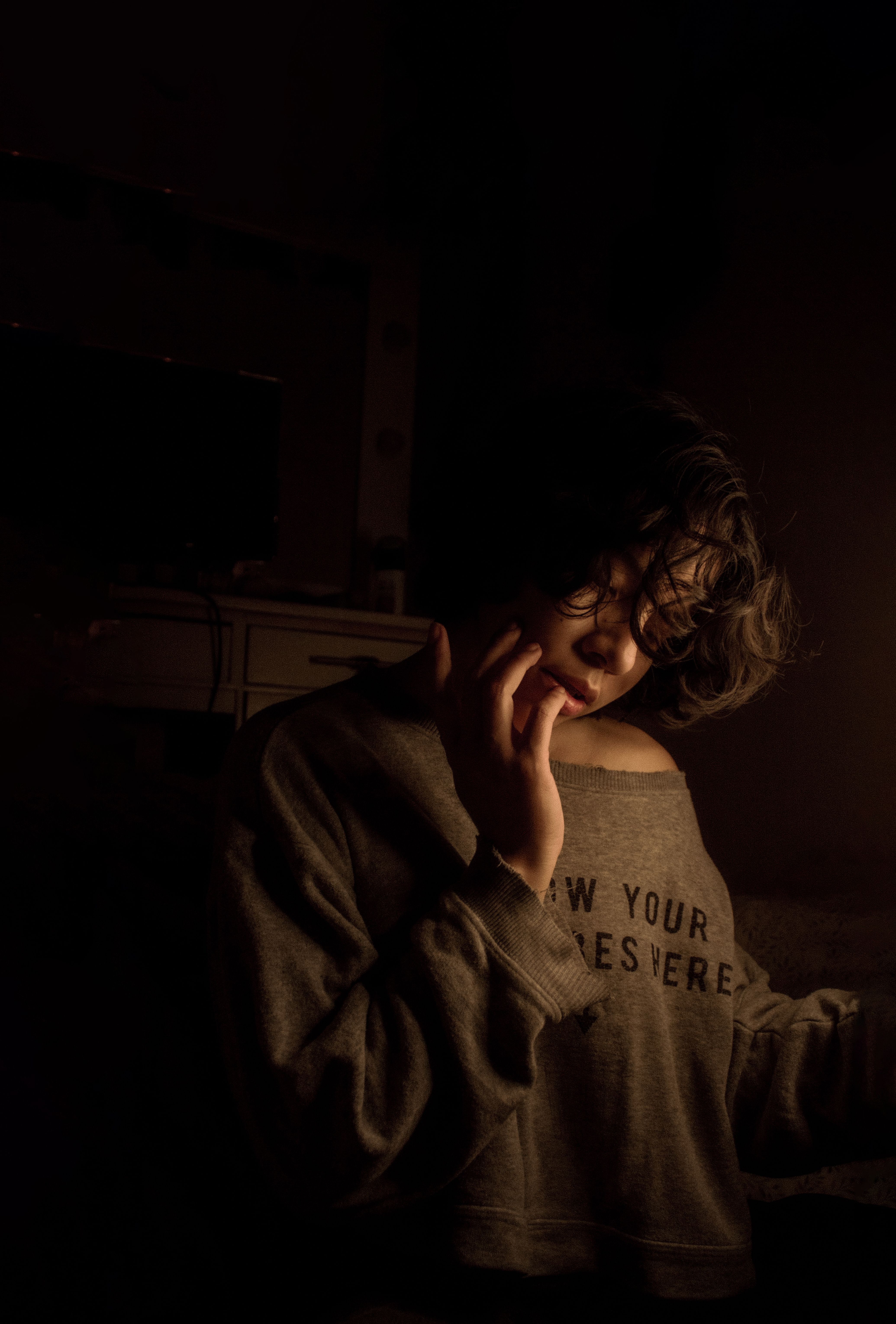 A woman in a dark room poses thoughtfully in soft, warm lighting.