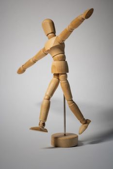 Wooden mannequin figure striking a playful and dynamic pose on a stick stand.