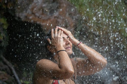 Free Woman embracing the rain outdoors with hands on head, enjoying water. Stock Photo