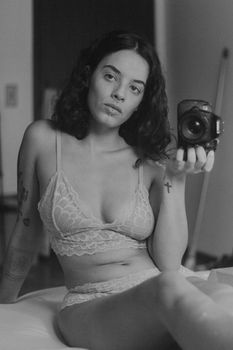 Artistic monochrome portrait of a woman in lingerie holding a camera indoors.
