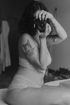 Artistic black and white self-portrait of a woman taking a photo with a camera.