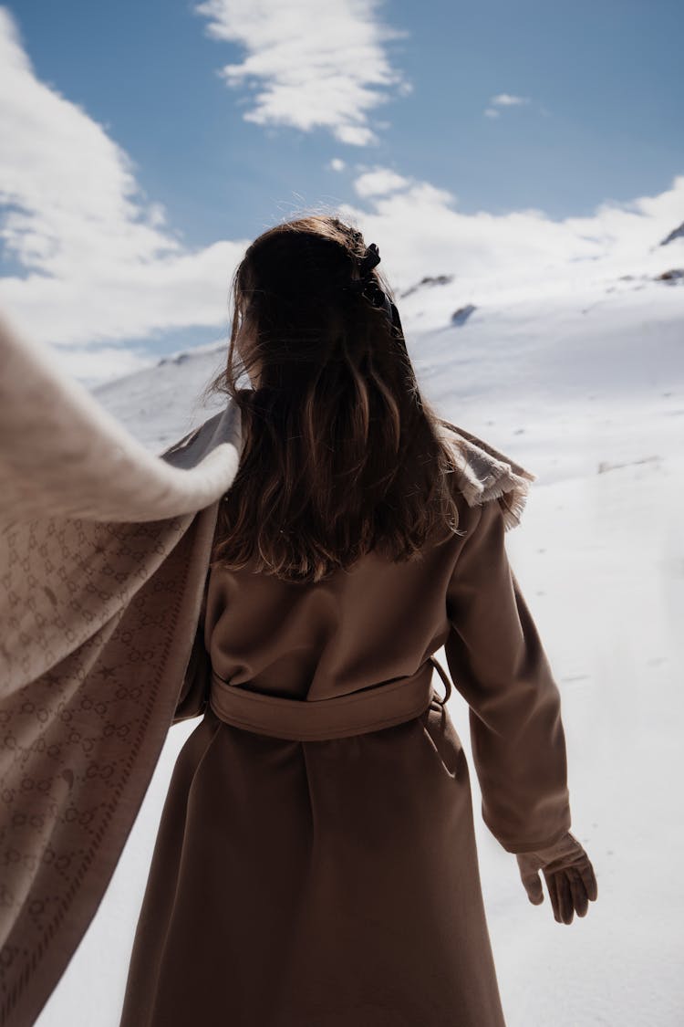 Woman Standing On Snowy Plains With Scarf Fluttering On Wind Behind Her