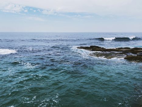 Calm ocean waves meet rock formations under a clear sky.