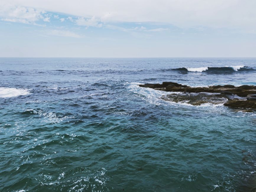 Calm ocean waves meet rock formations under a clear sky.